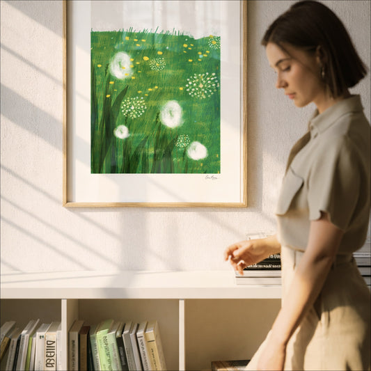 Resting Field art print above a bookshelf in a bright white room with a woman walking by, OAM Studio. Woman looking at a framed artwork of dandelions on a wall.
