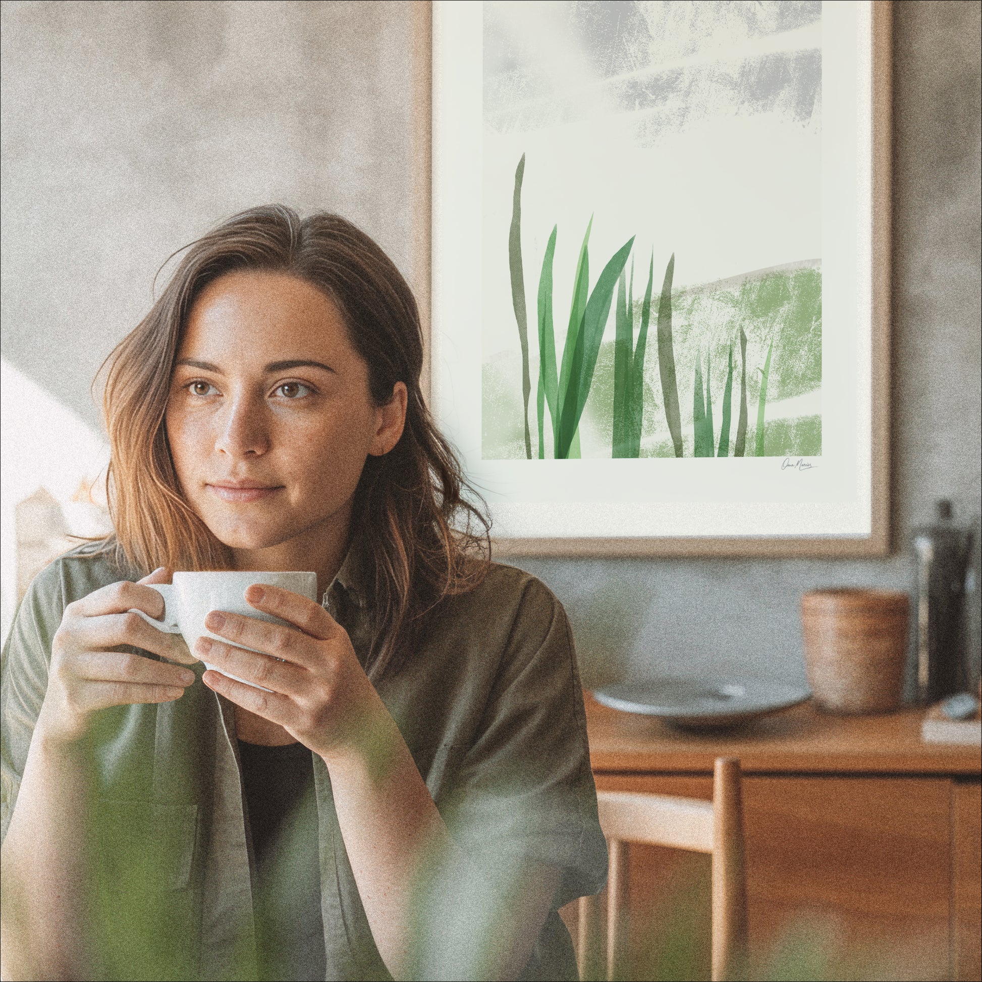 Woman holding a mug in a cozy room with a painting on the wall. Held by the Field art print leaning in a warm wooden interior, OAM Studio minimalist wall art