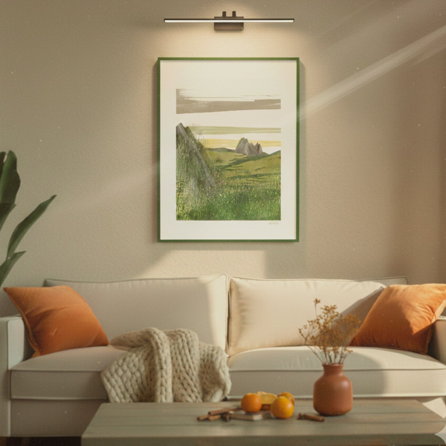 Open Field art print lying flat on a white surface next to a green plant, OAM Studio Living room with a beige sofa, orange cushions, and a framed landscape painting on the wall.