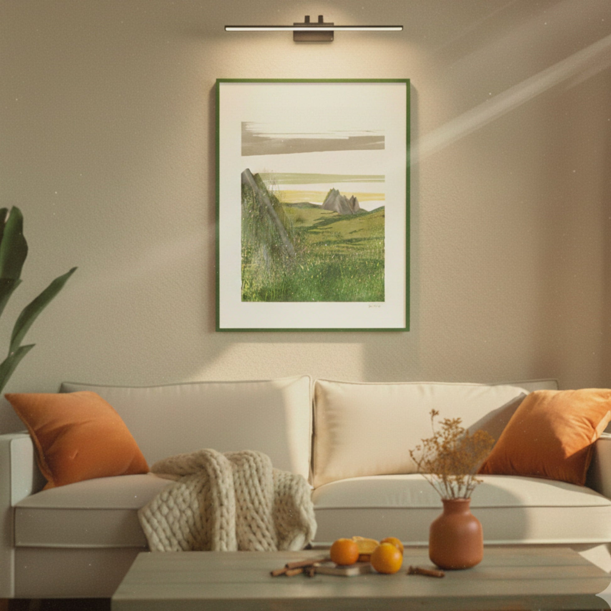 Open Field art print lying flat on a white surface next to a green plant, OAM Studio Living room with a beige sofa, orange cushions, and a framed landscape painting on the wall.