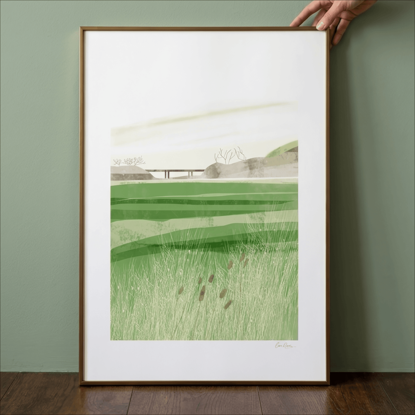 Framed artwork of a green landscape held by a hand against a green wall.