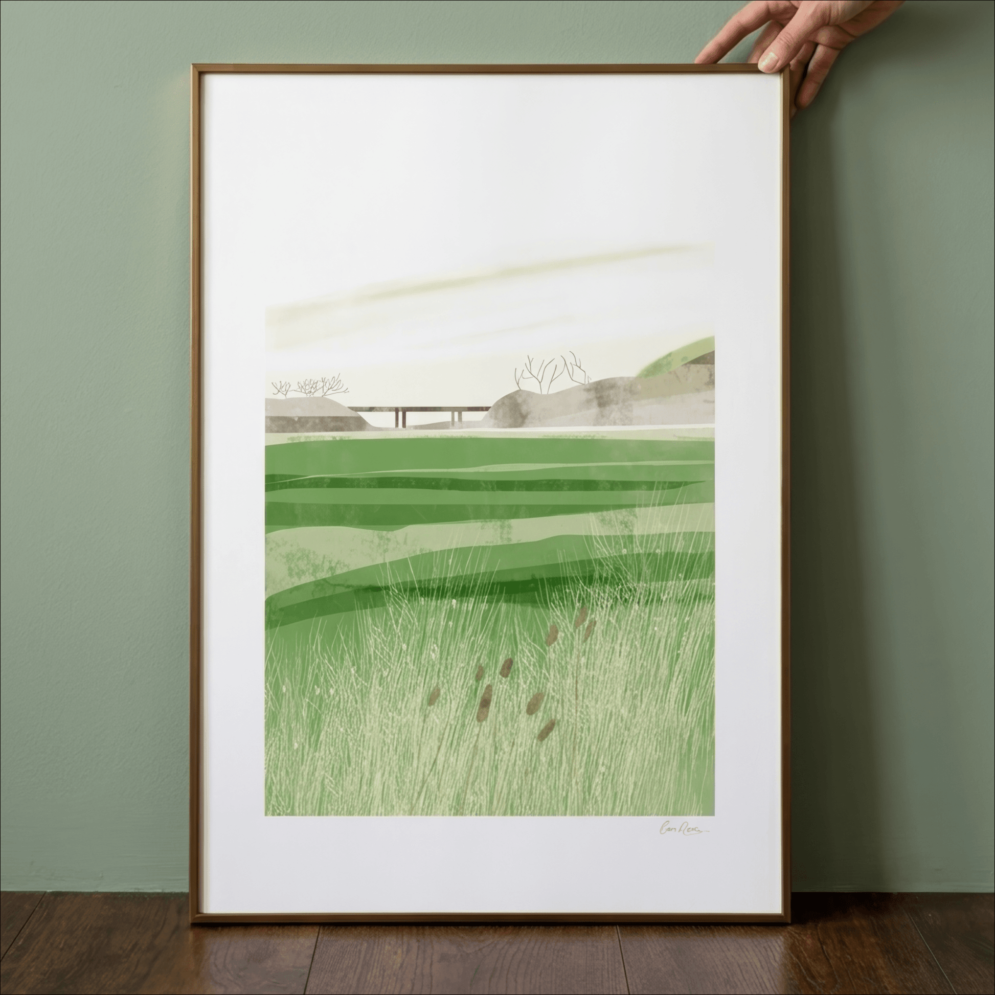 Framed artwork of a green landscape held by a hand against a green wall.