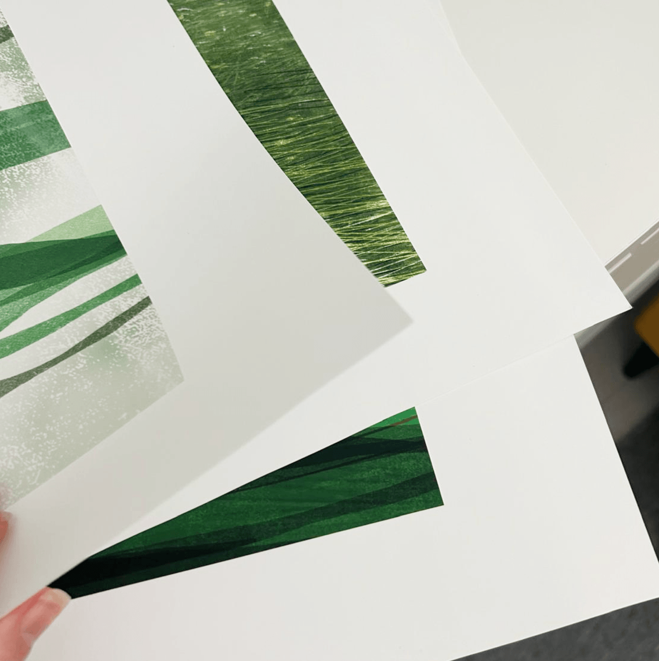 Green textured paper strips being held over a white surface with a tool on the side.